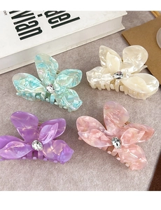 Close-up of four acetate flower hair claws with rhinestones in pastel iridescent colors