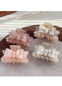 Detail of four acetate bow hair claws in marble and pearlescent finishes on a textured background