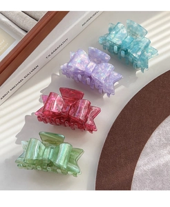 Detailed macro of acetate bow hair claws in various pearlescent colors on a wooden tray