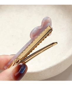 Détail d'une barrette en métal doré avec un papillon en résine aux reflets marbrés violets