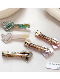 Détail de pinces à cheveux en acétate en forme de cœur avec strass et clips dorés