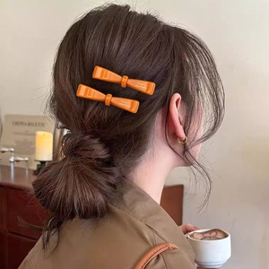 Paire de barrettes à cheveux nœud orange brillant portées sur une coiffure tressée