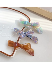 Detail of three acetate bow hair clips in marble and amber colors on a ceramic tray