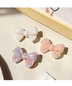 Trois barrettes nœud en acétate blanc perle et motifs marbre rose sur un bureau doux