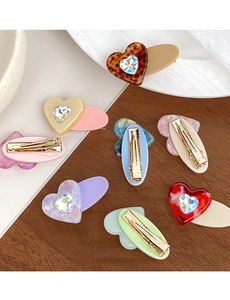 Detail of heart hair clips with resin patterns and rhinestone inlay on gold duckbill clip