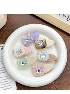Détail de barrettes chat en acétate avec strass incrustés sur une assiette blanche