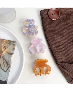 Three acetate hair claw clips in purple, pink marble and amber displayed on velvet