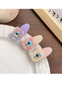 Détail de trois barrettes chat en acétate avec strass incrustés posées sur une assiette