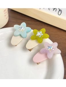 Close-up of three colorful acetate flower hair clips with rhinestones on a white plate