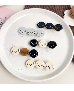 Detail view of five assorted puppy-shaped acetate hair clips in a white ceramic dish
