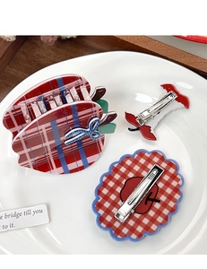 Three-piece hair clip set with red plaid apple shapes on white ceramic plate
