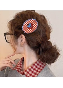 Detail of red plaid apple-shaped hair claw clip with blue bow on wavy hair