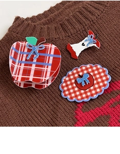 Detailed view of red plaid apple hair claw and clips on a warm autumn knitted sweater