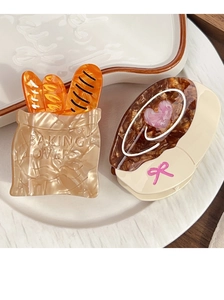 Detail of bread-shaped acetate hair claw clips with Baking Lovers text on wood table