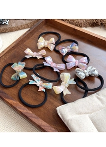 Close-up of handmade acetic acid bow hair ties on a wooden tray with golden engraving