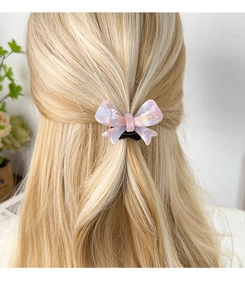 Detail of a pink acetate bow hair tie with marble texture on a model's hair
