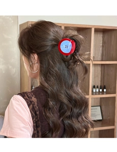 Détail d'une pince à cheveux en forme de bouton rouge et bleu sur cheveux bouclés