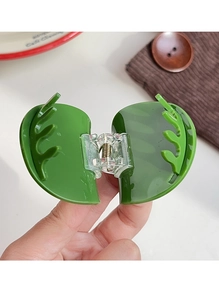 Détail d'une pince à cheveux en forme de feuille verte en plastique brillant avec un ressort