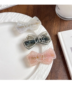 Detail of three marble textured bow hair clips in grey and pink on a ceramic plate