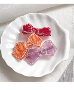 Detail of bow-shaped acetate hair clips in red, orange, and purple on shell tray