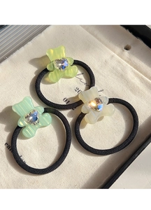 Close-up of three elastic hair ties with bear charms in green, yellow, and white colors