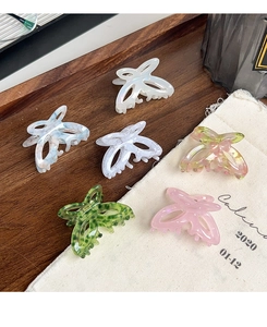 Detail view of butterfly hair claws in six glossy acetate colors on a textured cloth