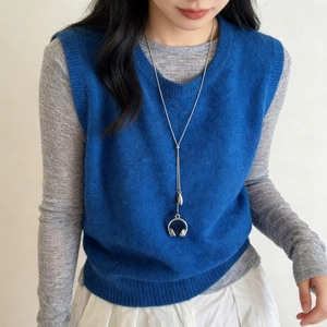 Silver headphone pendant necklace worn over a blue V-neck knit vest and gray long sleeve