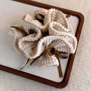Détail d'un chouchou en maille gaufrée beige avec ruban en satin marron foncé sur support
