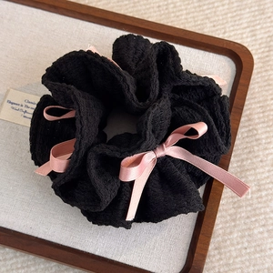 Gros plan d'un chouchou plissé noir avec des nœuds en satin rose sur un plateau de luxe