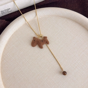 Detail of a brown flocked horse pendant on a gold snake chain with a tiger eye bead