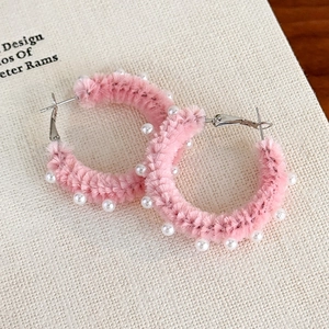 Gros plan sur des créoles en peluche rose avec perles blanches sur papier texturé