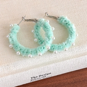 Vue macro de boucles d'oreilles créoles pelucheuses vert menthe avec perles blanches