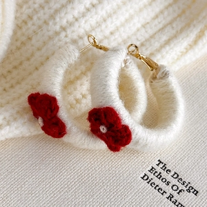 Détail de boucles d'oreilles créoles en laine crème avec fleur au crochet rouge