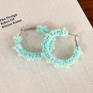 Détail de créoles en peluche vert menthe avec d'élégantes décorations en perles blanches