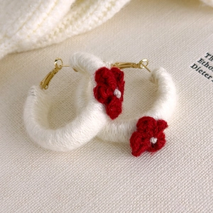 Détail de boucles d'oreilles créoles en laine blanche avec petites fleurs rouges