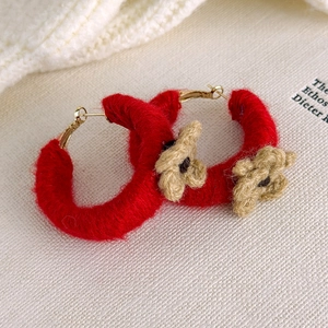 Détail de créoles en C enveloppées de fil rouge avec fleurs au crochet sur tricot blanc