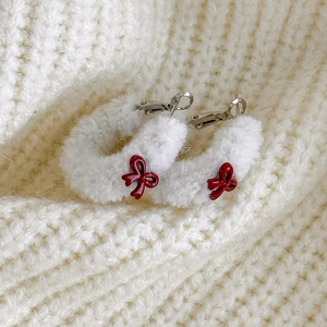 Détail de boucles d'oreilles en peluche blanche avec nœuds rouges sur fond de pull en tricot
