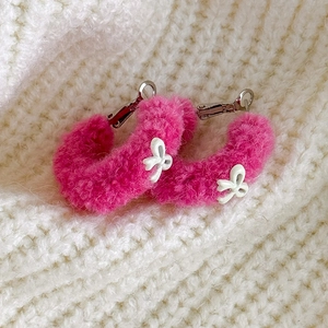 Gros plan d'une boucle d'oreille en peluche rose rouge avec nœud blanc sur tricot chaud
