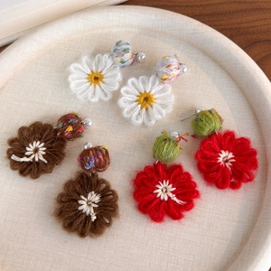 Detail of three pairs of hand-knitted flower earrings with pearls on a wooden tray