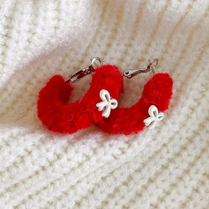 Gros plan de boucles d'oreilles en peluche rouge en forme de C avec nœud blanc doux