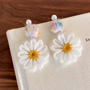 Detail of handmade knit daisy earrings with colorful plush balls and white pearls