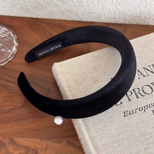 Detail view of handmade black velvet headband with elegant pearl accent and textile label