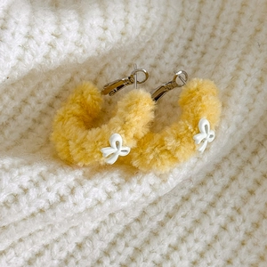Gros plan de créoles en peluche jaune avec détails nœuds blancs sur fond en tricot doux