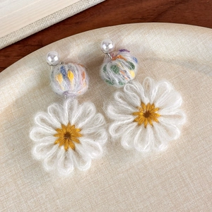 Detailed close-up of knitted daisy earrings with colorful wool balls and pearls