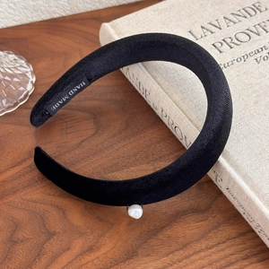 Close-up of vintage black velvet headband with pearl detail and handmade label on wood