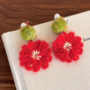 Detailed close-up of handmade red crochet flower earrings with white pearl accent