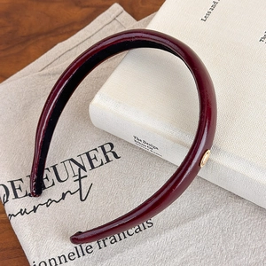 Detail view of burgundy leather headband texture with a small gold metal decorative buckle