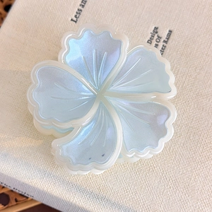 Dettaglio della pinza per capelli a fiore azzurro con finitura perlata su sfondo di tessuto