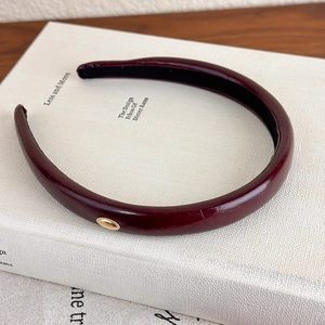 Vintage burgundy faux leather headband with gold metal logo on a book display
