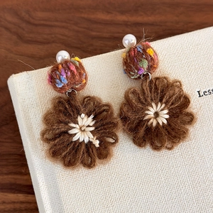 Macro detail of handmade winter flower earrings with pearls and mixed wool textures
